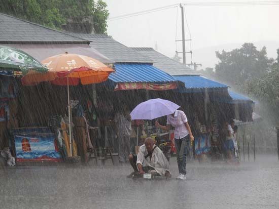 A young Chinese girl holds an umbrella for an old disabled beggar during a rainstorm.