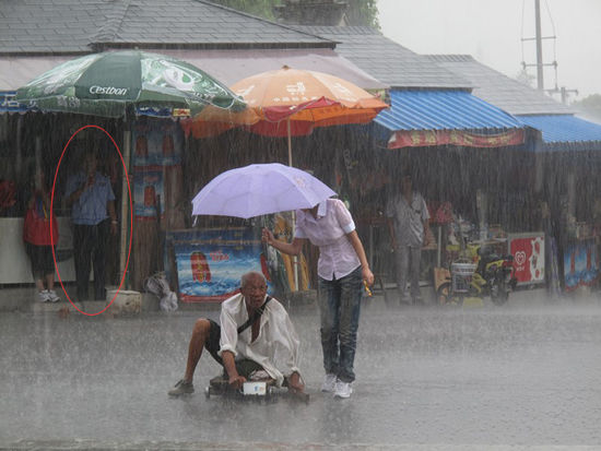 A Chinese girl holds a purple umbrella for a disabled beggar during a rainstorm.