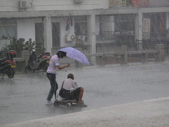 A girl walks beside a disabled beggar crawling home on a makeshift wooden cart in the rain.
